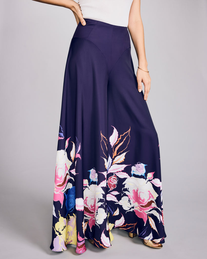 Ultra wide-legged trousers from D2Line are crafted from a rich aubergine purple luxury polyester with floral patterning at the bottom in shades of pink, blue, white, purple and chartreuse 