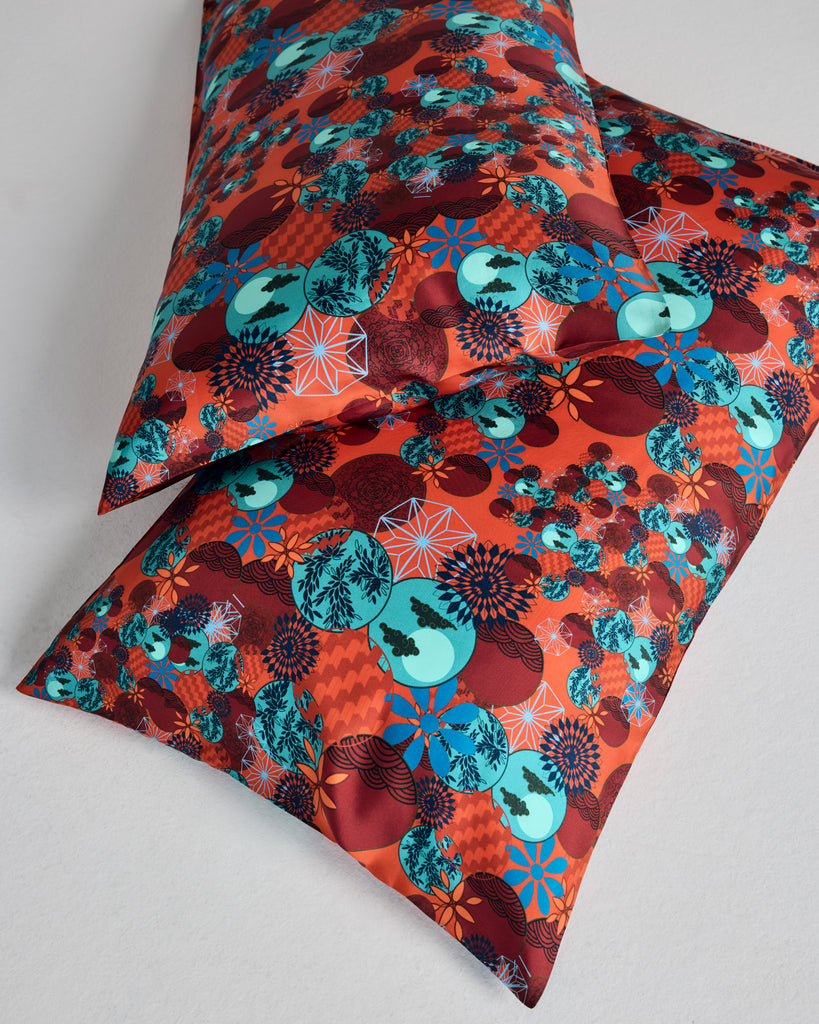 Tama Coral Silk pillowcases from Karma on the Rocks are crafted from a luxurious coral red silk twill with a a Japanese-inspired print showcasing clouds, suns, foliage and geometric designs in shades of red, teal and blue
