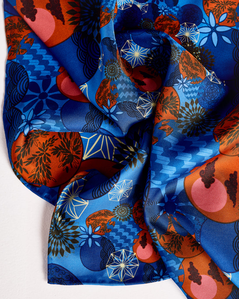 Classic Tama Blue square scarf from Karma on the Rocks is crafted from a Japanese-inspired print showcasing clouds, suns, foliage and geometric designs in shades of blue, red, black and gold 