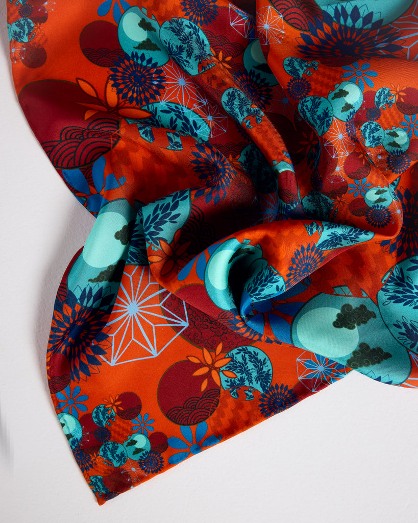 Classic Tama Coral square scarf from Karma on the Rocks is crafted from a Japanese-inspired print showcasing clouds, suns, foliage and geometric designs in shades of coral, red, teal and blue